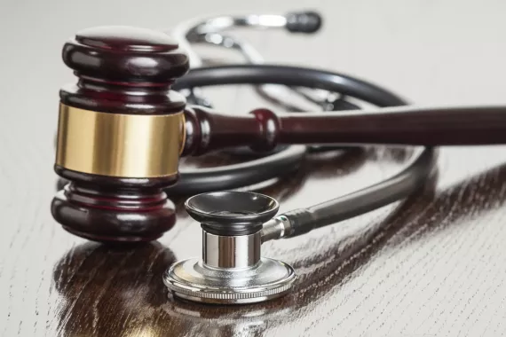 A stock image of a judge's gavel and a stethoscope lying on a wooden desk.